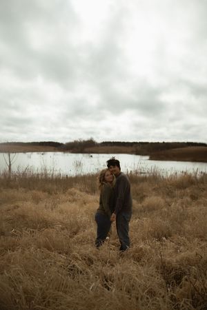 Two people share a tender moment in a brown autumn field landscape.