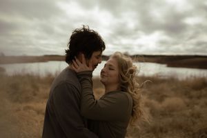 Two people share a passionate embrace against a dramatic cloudy sky.