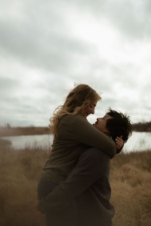 An intimate embrace between two people against a moody lakeside backdrop with cloudy skies.