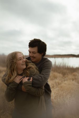 Two people share playful moments in a field under overcast skies.