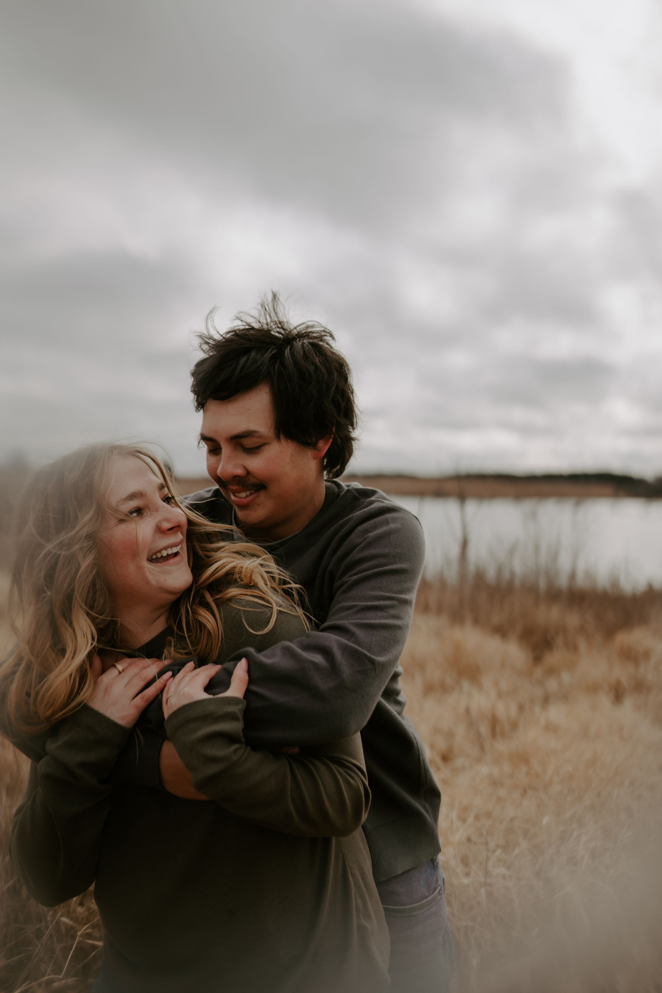 A playful moment between a couple laughing together in a autumn field.