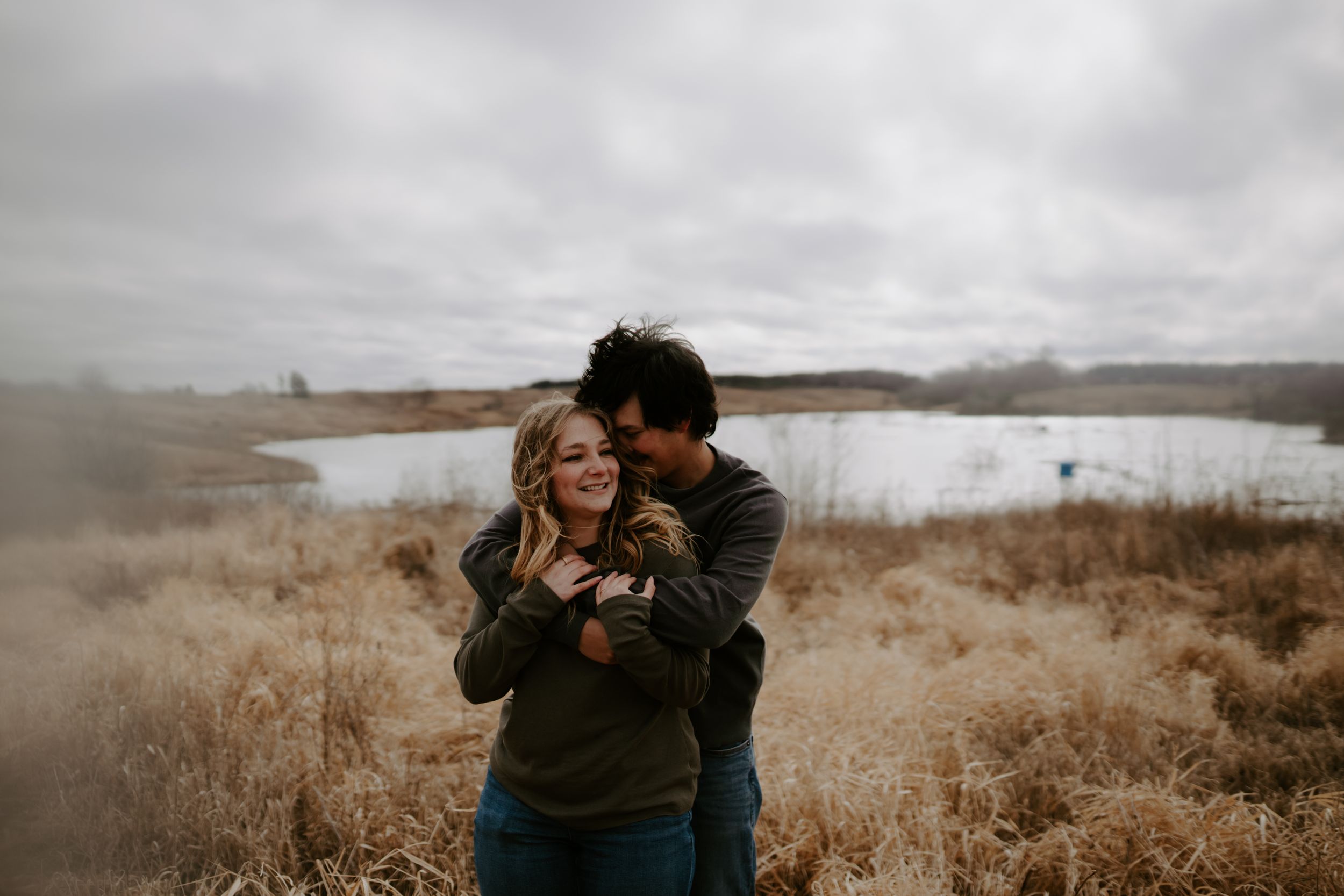 A romantic embrace captured in a rustic field with moody overcast skies.