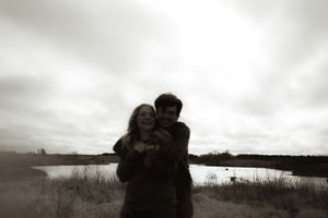 A black and white photo captures an intimate moment between two people by a lake.