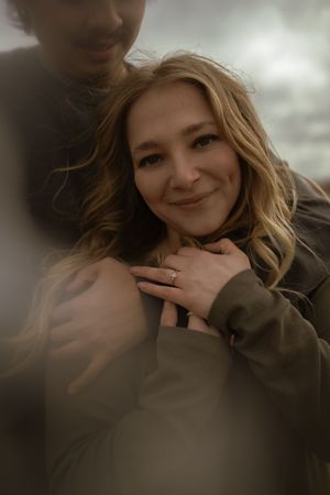 A close-up shot shows a woman with blonde waves smiling while displaying her ring.