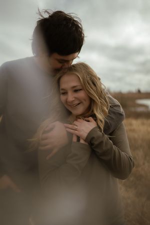 Intimate moment between couple embracing in a field under cloudy skies.