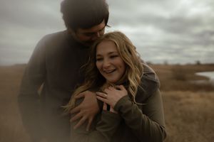 Couple sharing tender moment outdoors with moody overcast sky in background.