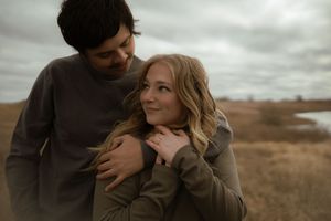 Candid shot of couple embracing in autumn field with overcast sky.