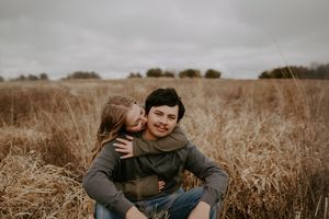 Couple sharing playful moments while sitting in tall grass field.