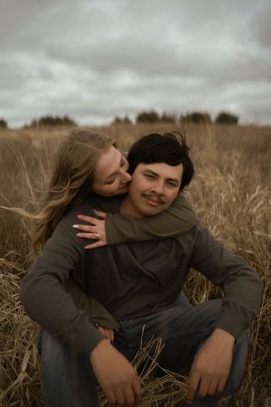 Intimate moment between couple in field with dramatic cloudy sky.
