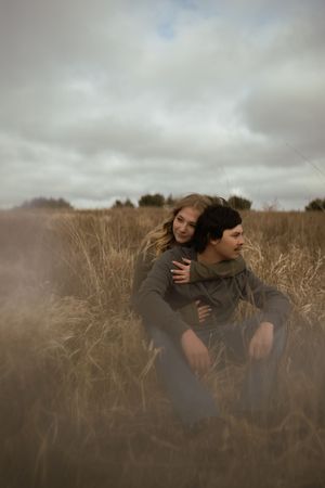 A couple embraces in a field of tall grass on an overcast autumn day.