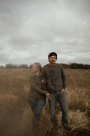 A couple playfully interacts in a rustic outdoor setting with cloudy skies.