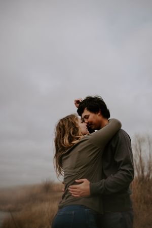Couple embracing in a field during an overcast autumn day.