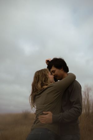 Two people share a romantic moment in a field under moody winter skies.