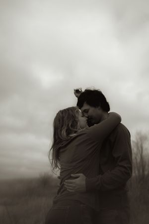 An intimate black and white portrait of two people embracing outdoors.