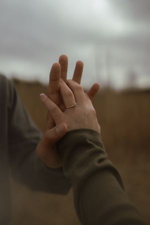 A hand wearing a wedding band reaches upward against an overcast sky.