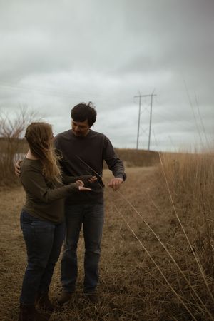 A couple interacts playfully in a field with power lines in the background.