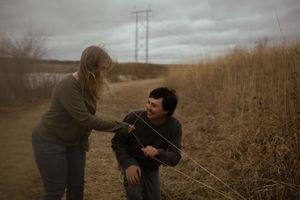 A couple shares a tender moment in a field of tall grass on an overcast day.