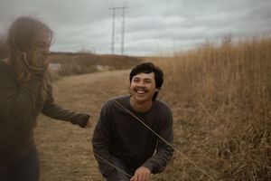 A joyful interaction between two people in a rustic outdoor setting with cloudy skies.