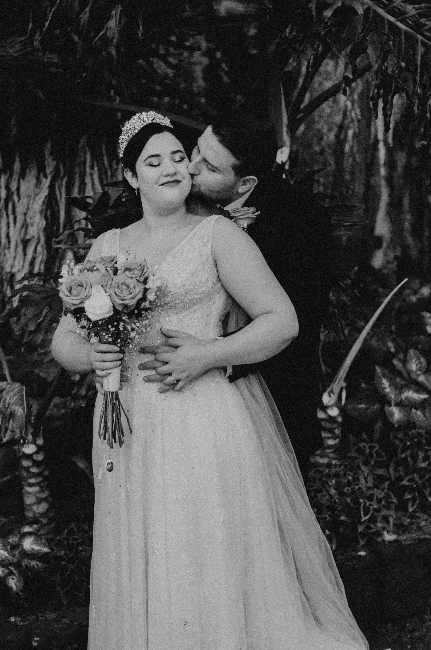 Black and white wedding photo capturing romantic moment between newlyweds in garden setting.