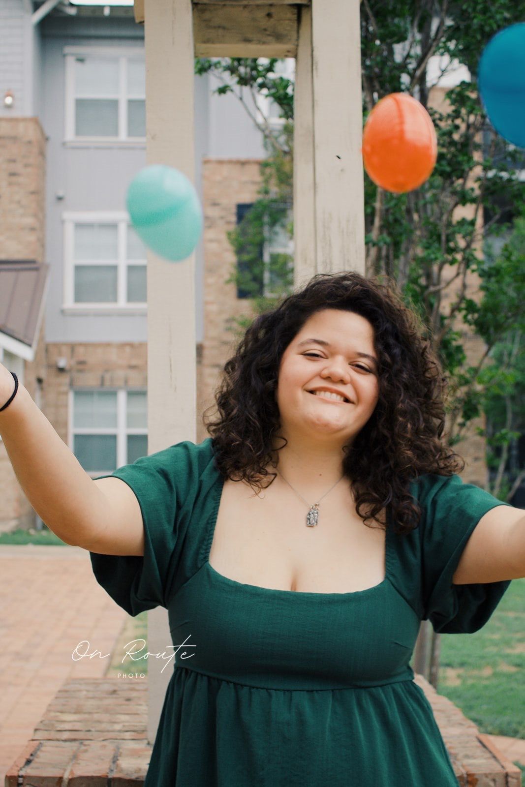 A joyful moment captured outdoors with festive balloons in orange, teal and blue colors against an apartment building backdrop.