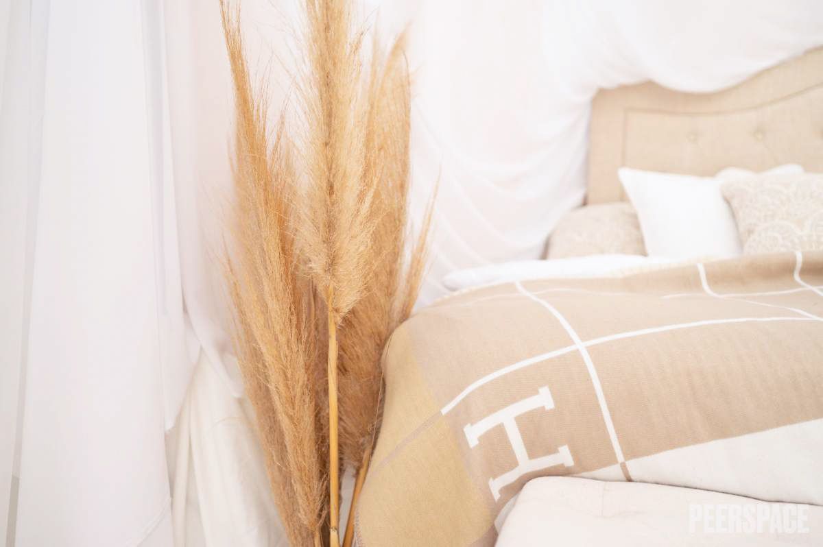 Cozy bedroom corner decorated with pampas grass and neutral toned bedding.
