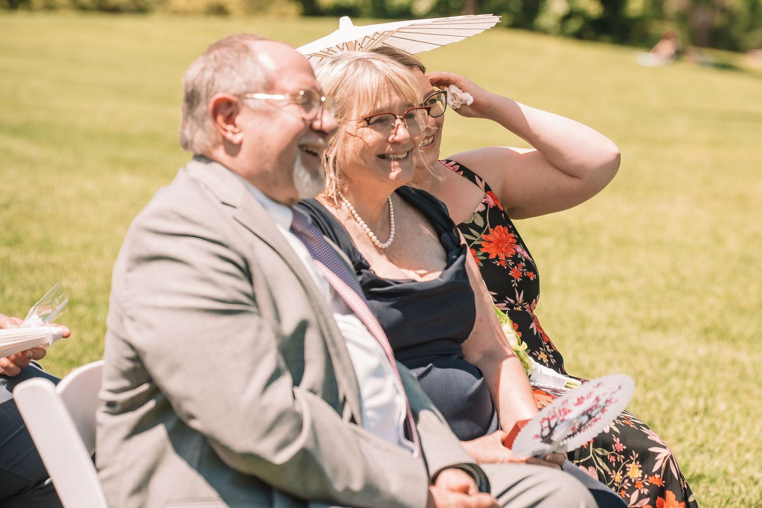 A couple sitting outdoors on a sunny day sharing a laugh together at a summer gathering.