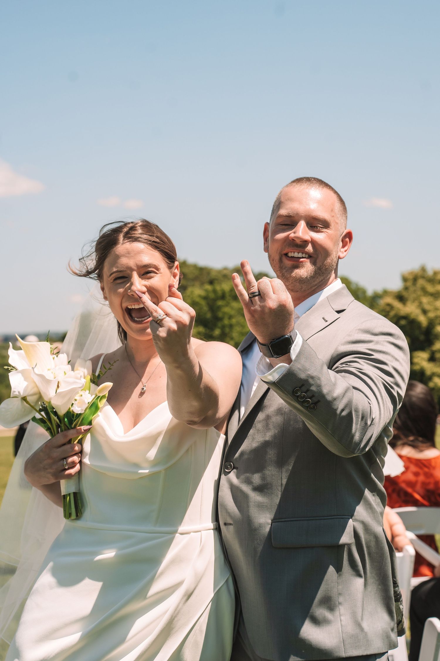 Newlywed couple celebrating with joyful expressions and white bouquet outdoors on their wedding day.