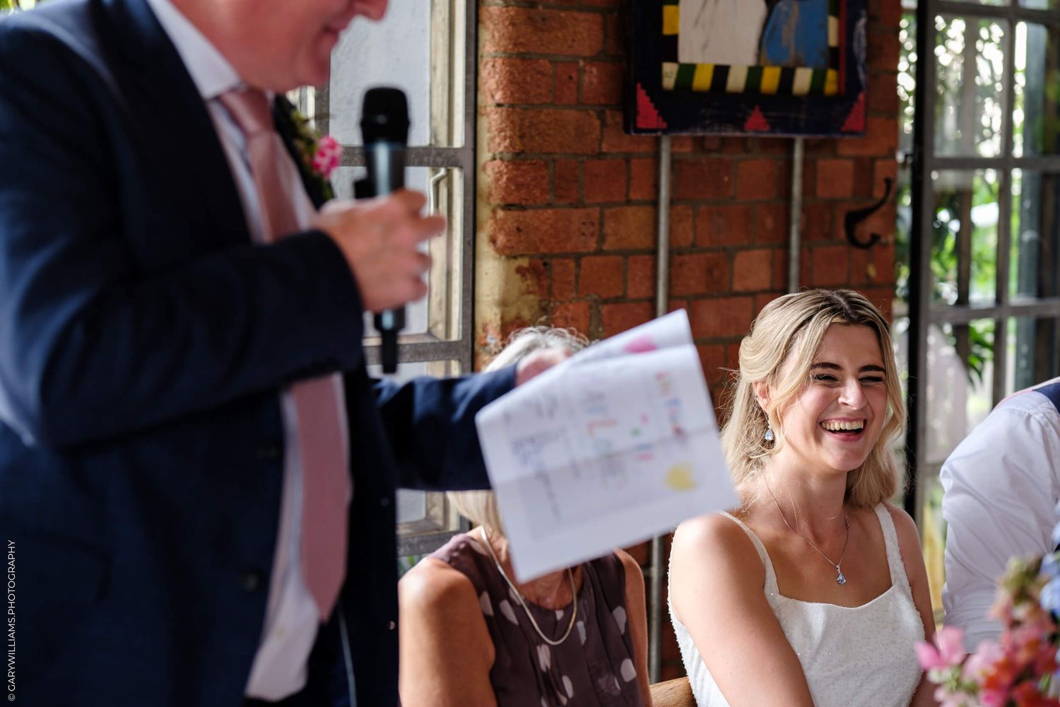 People enjoying an indoor wedding reception celebration with speeches at a rustic brick venue.