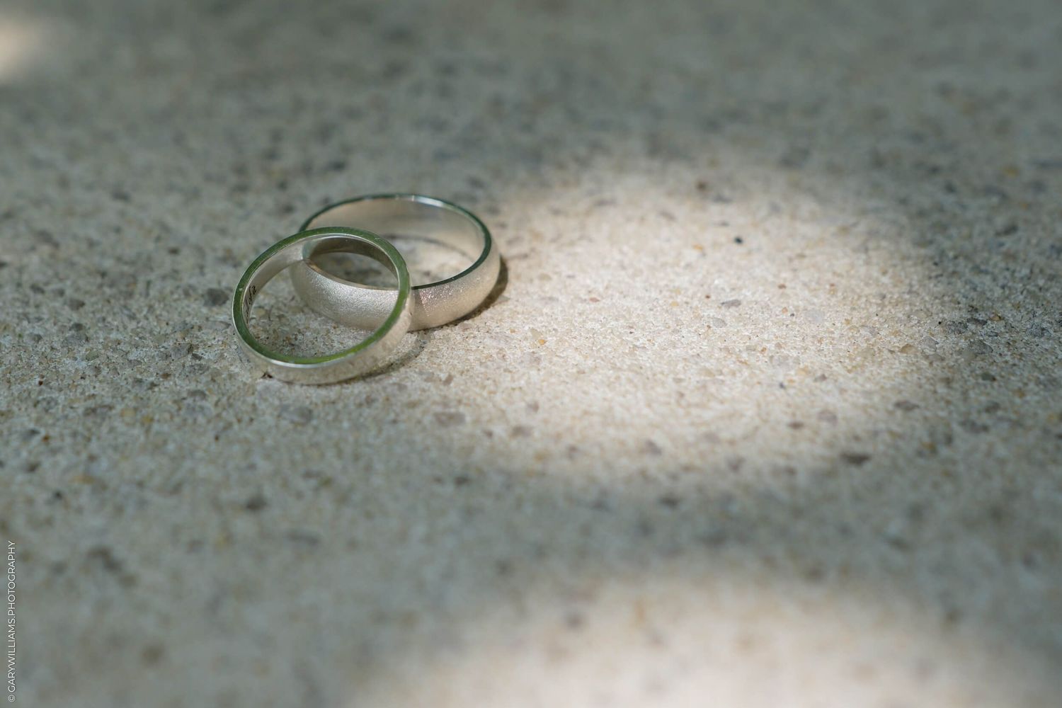 Two simple gold wedding rings rest side by side on a textured stone surface in soft lighting creating a romantic composition.