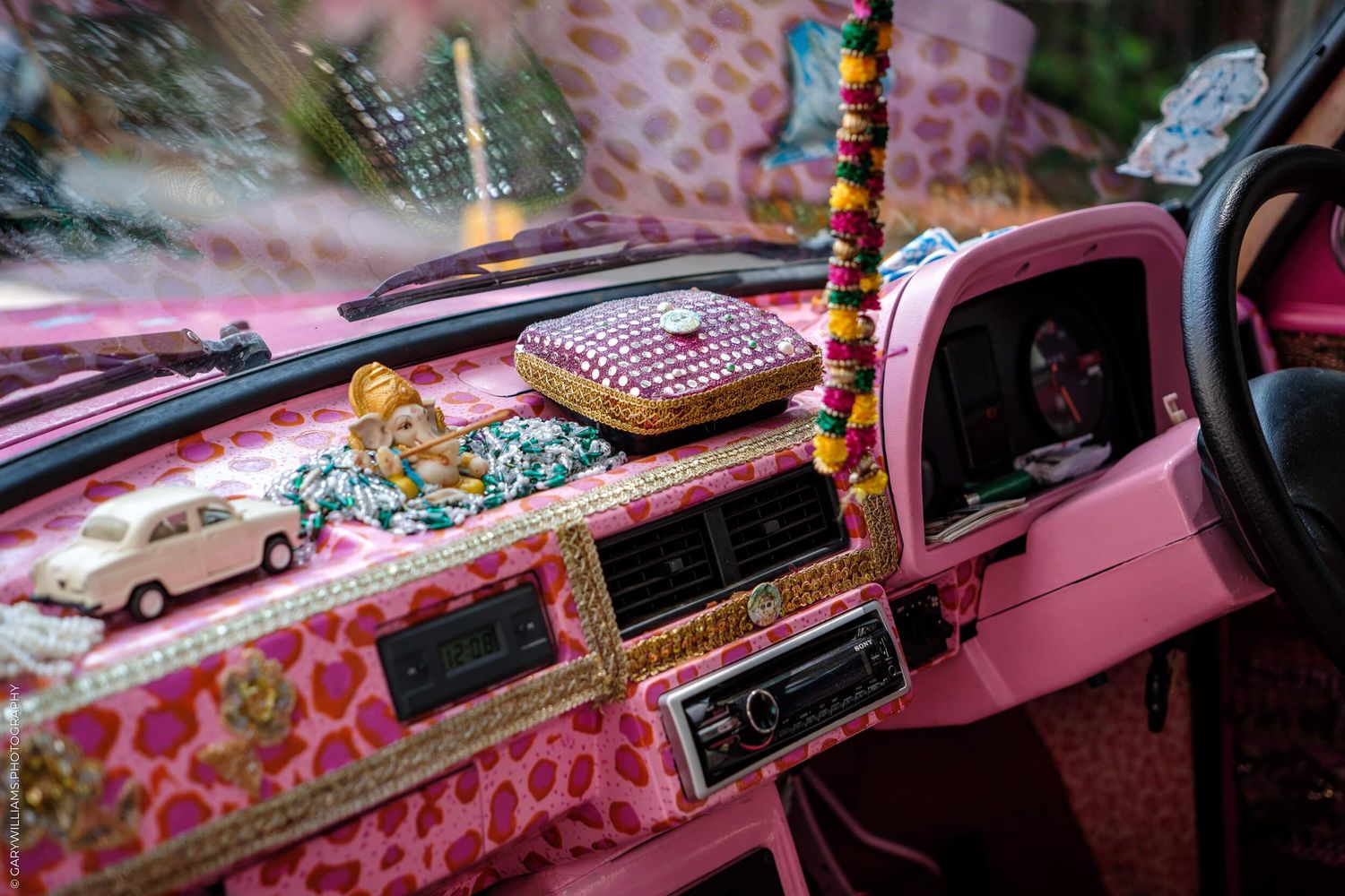 Dashboard of a pink car decorated with colorful toys and accessories showing a kitsch or kawaii aesthetic style.