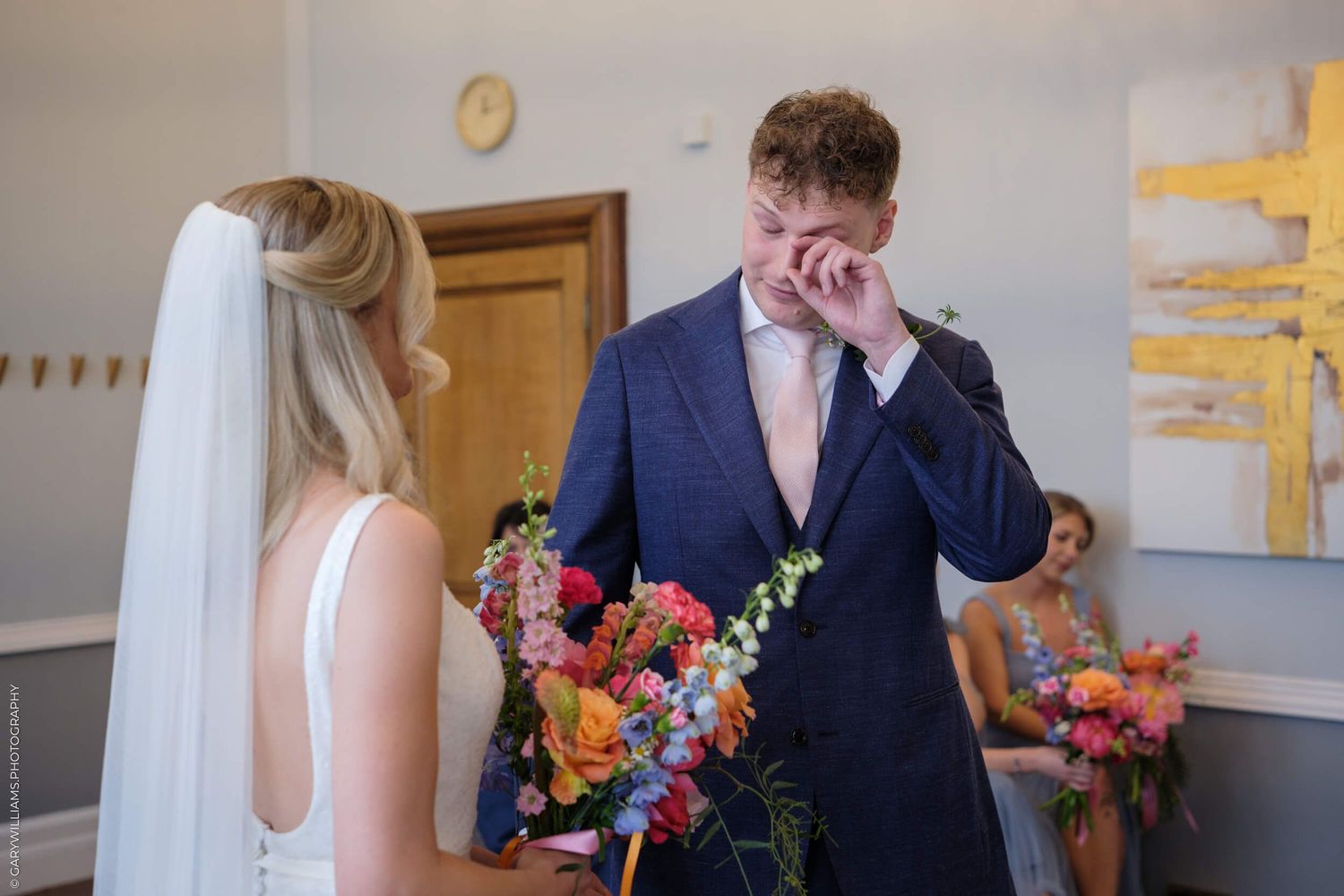 An emotional first look moment as two wedding participants share a private encounter with vibrant flowers in a bright room.