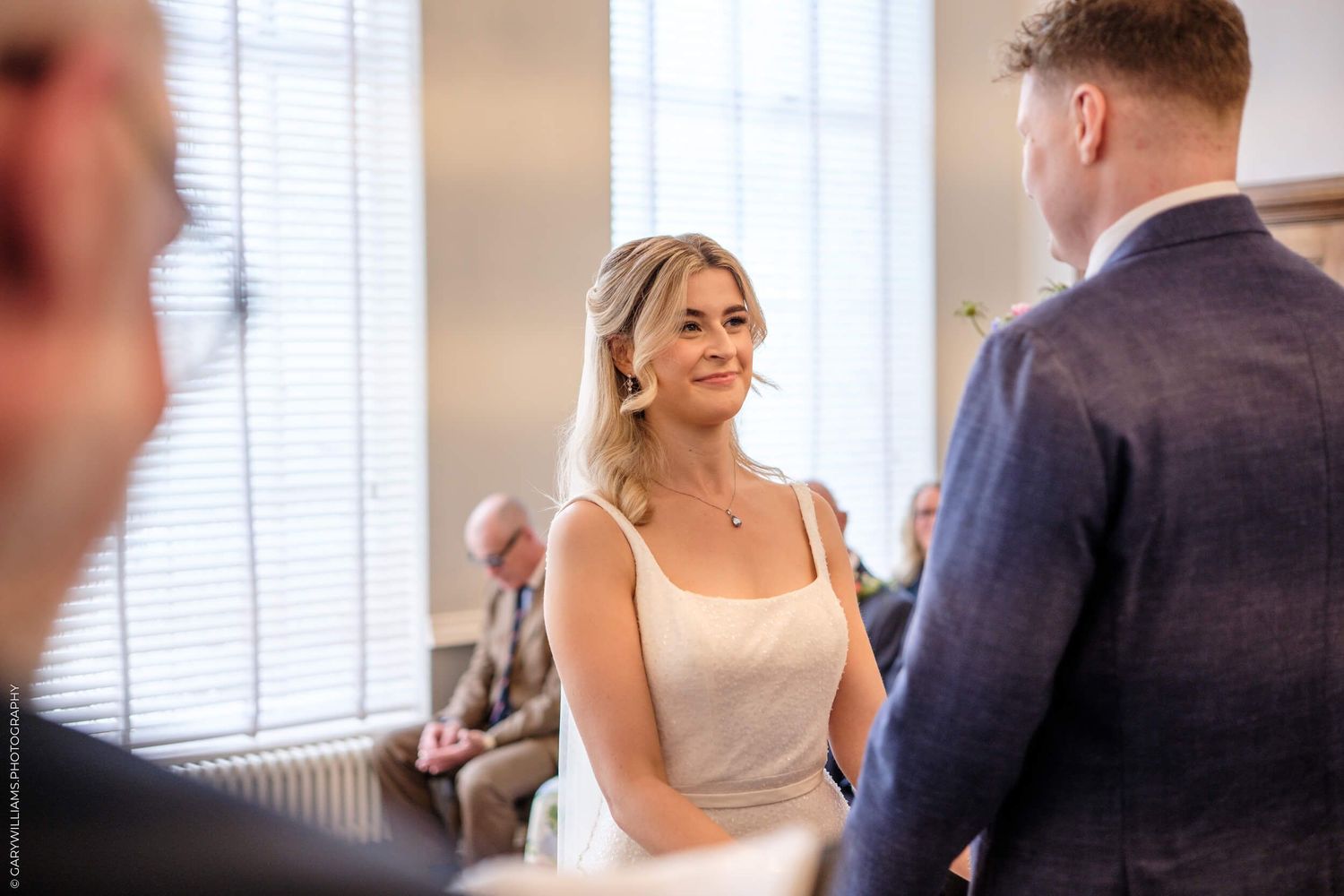 A wedding ceremony candid moment showing a couple exchanging vows in a sunlit indoor venue.