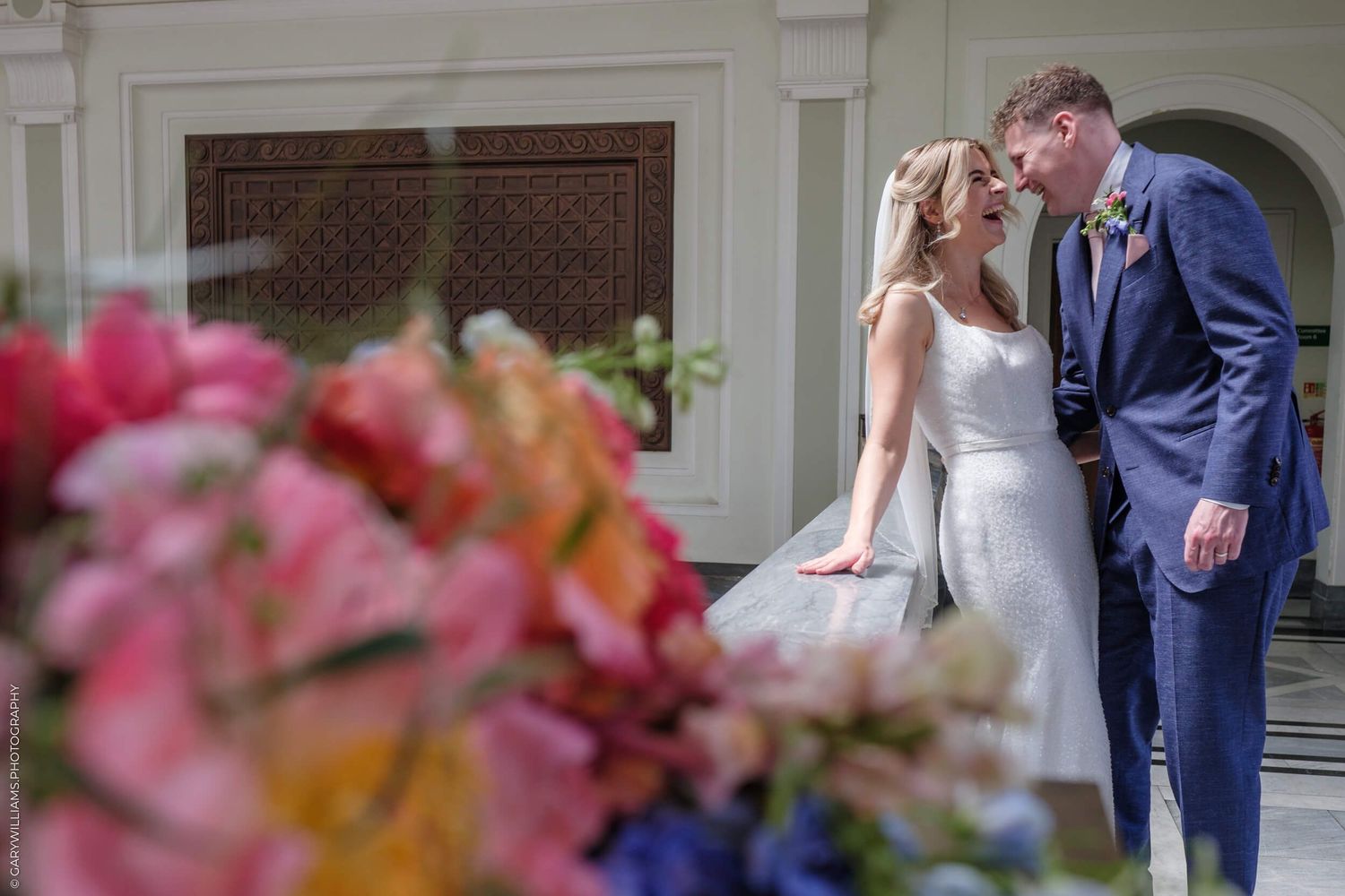 Couple walking up elegant marble stairs at a wedding venue with pink flowers in foreground.