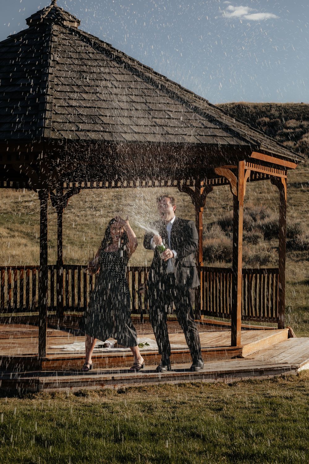A couple dances together under a wooden gazebo in the rain on a hillside.
