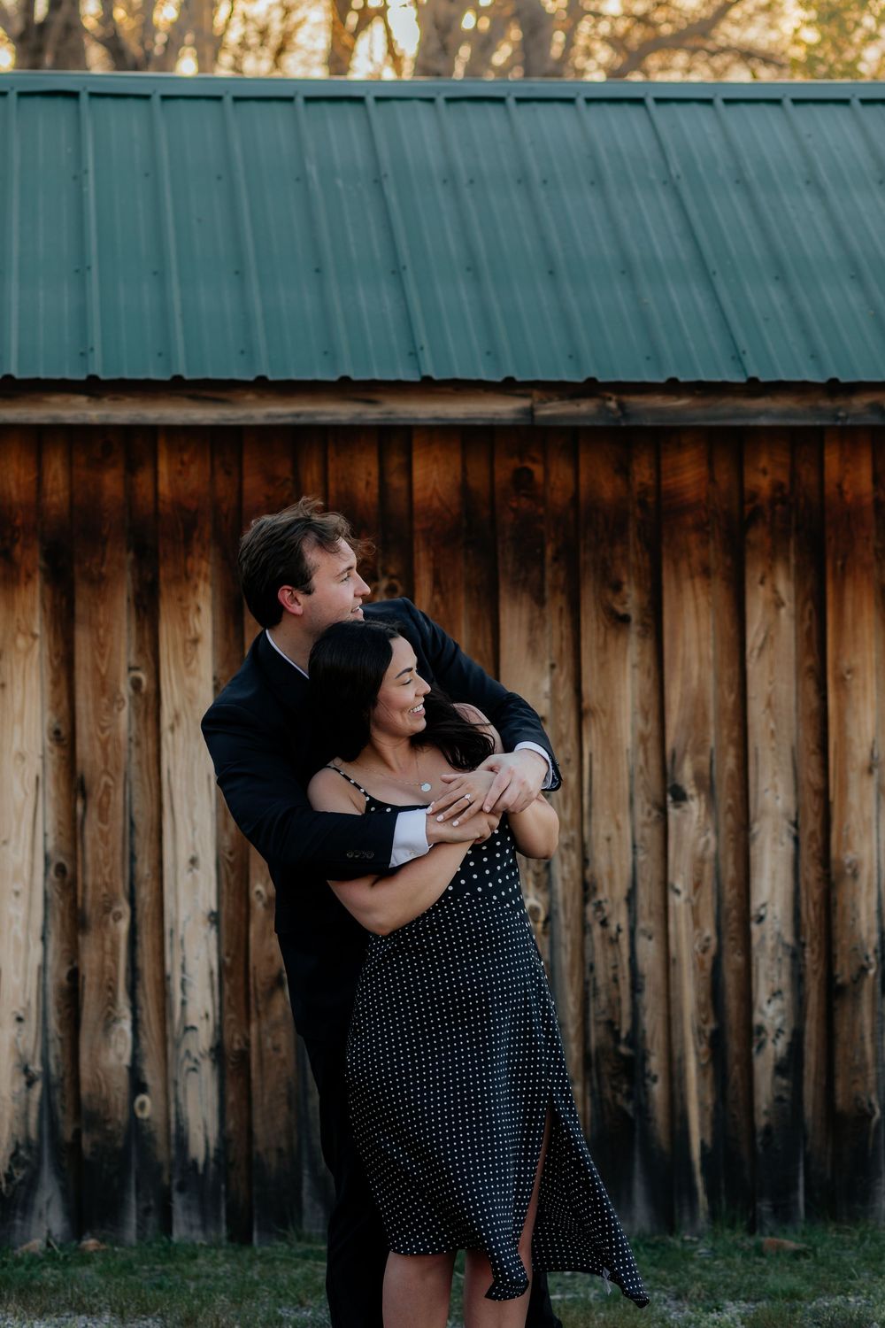 A couple embraces against a wooden fence in soft golden light.