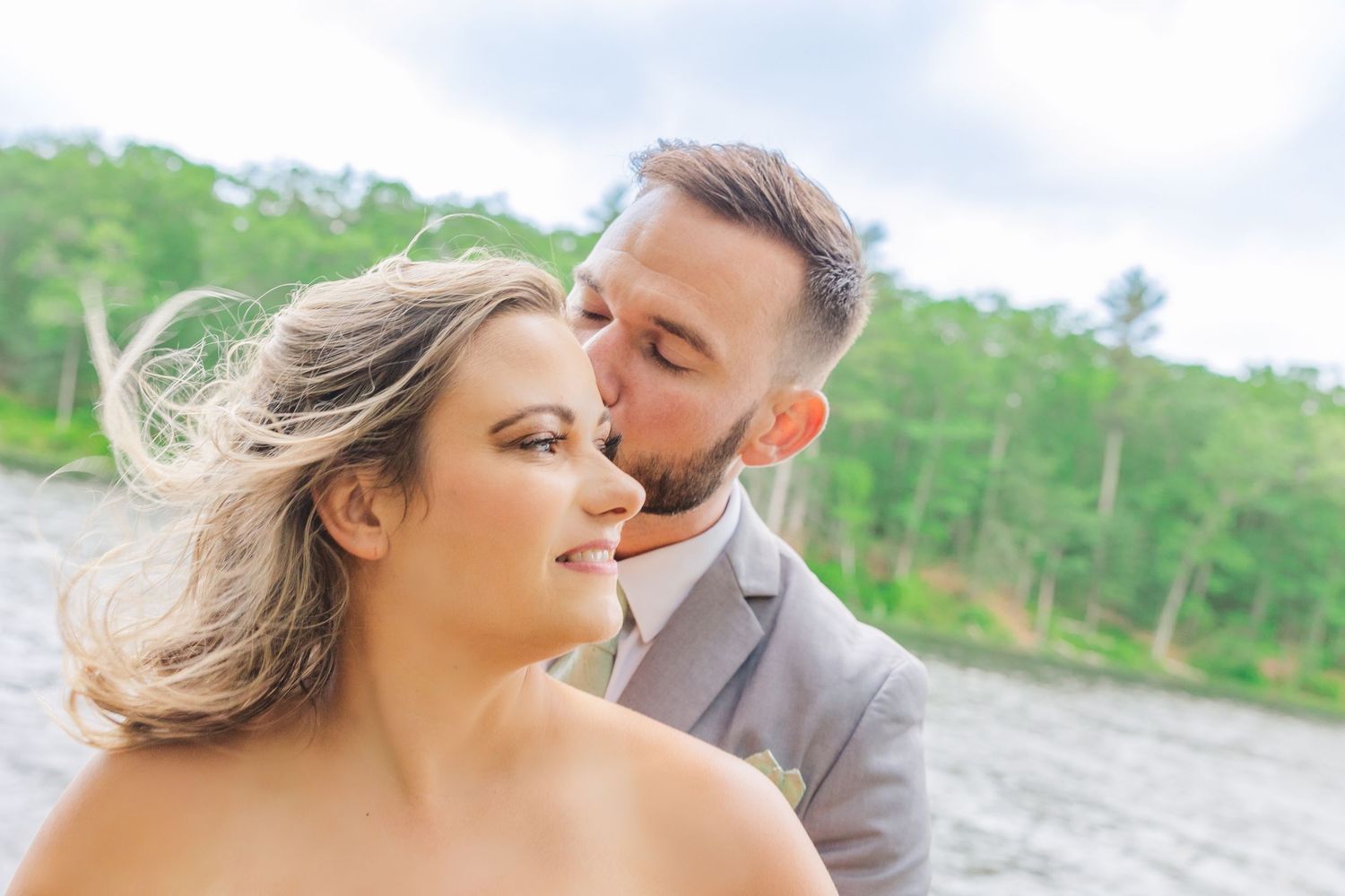 A tender moment between a couple on their wedding day with sunlight and green trees in the background.