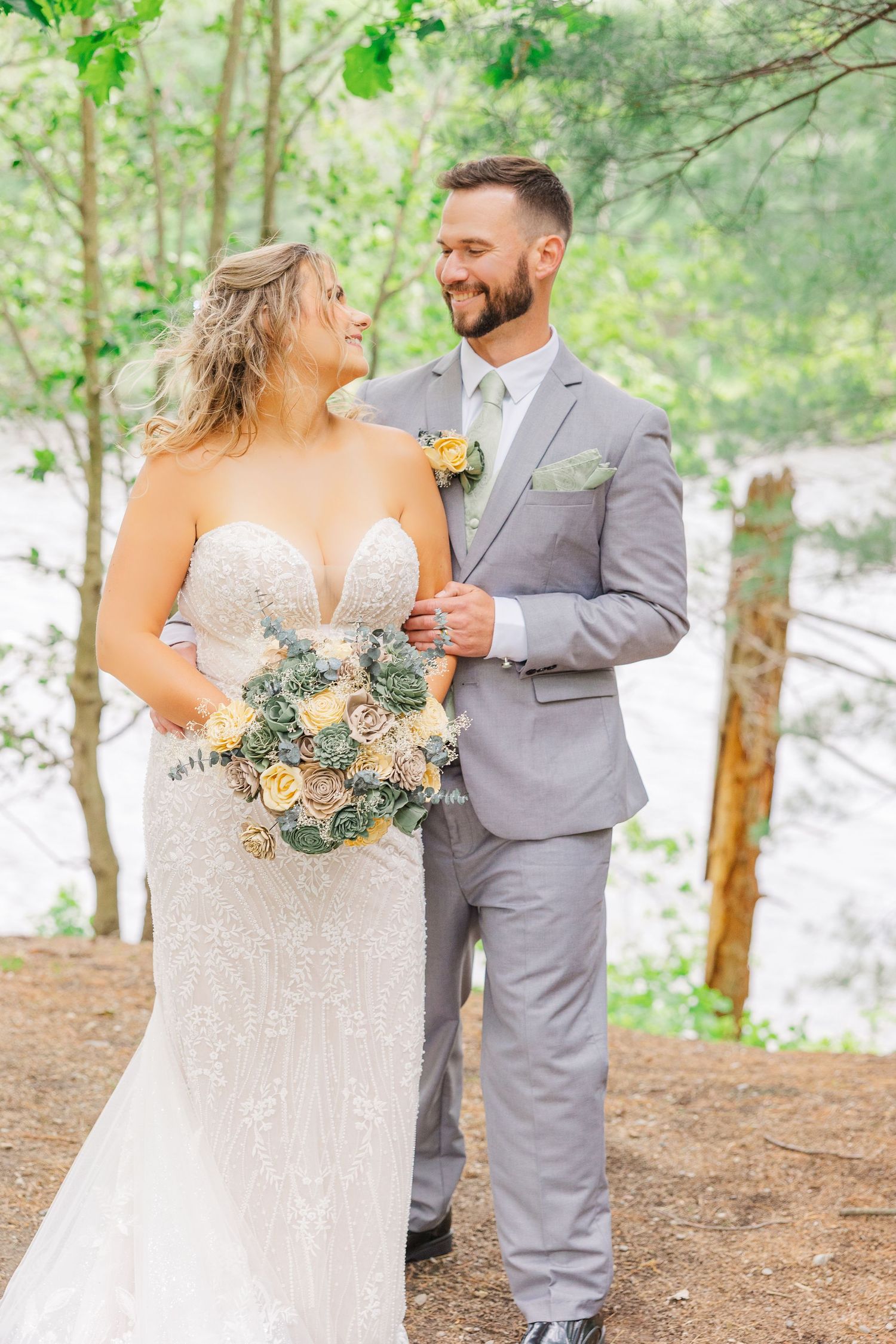 A joyful wedding couple shares a tender moment in a forest setting, with the bride holding a peach-colored bouquet.