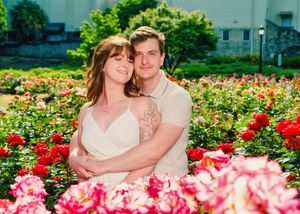 A couple embraces in a garden filled with vibrant pink roses on a sunny day.