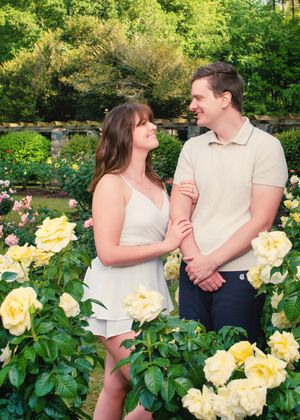 A couple shares a tender moment among blooming yellow roses in a lush garden setting.