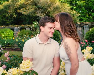 A romantic couple shares an intimate moment together in a lush garden filled with blooming yellow roses and greenery.