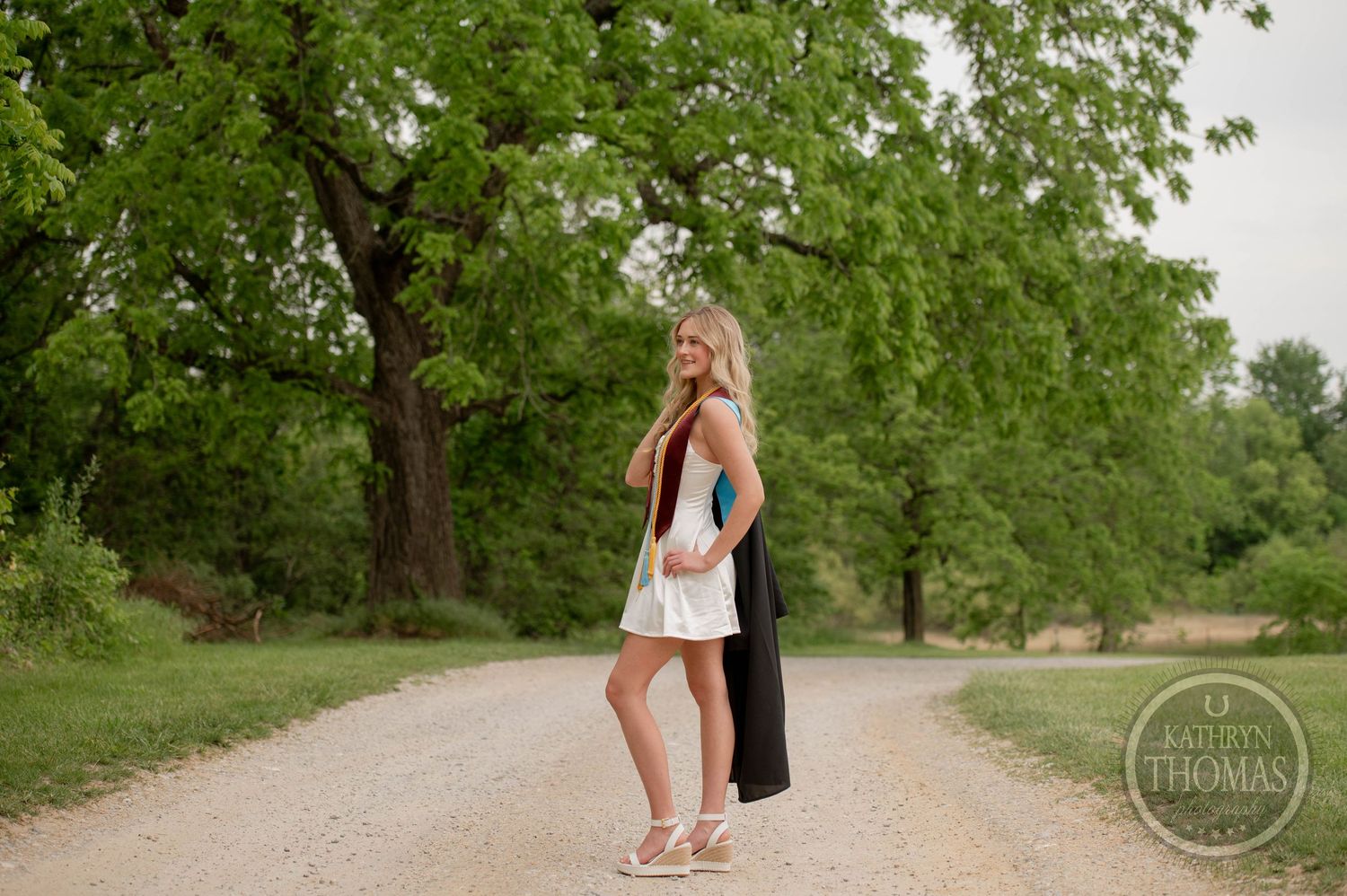 An outdoor engagement photoshoot session taking place on a tree-lined path in a lush green park setting.