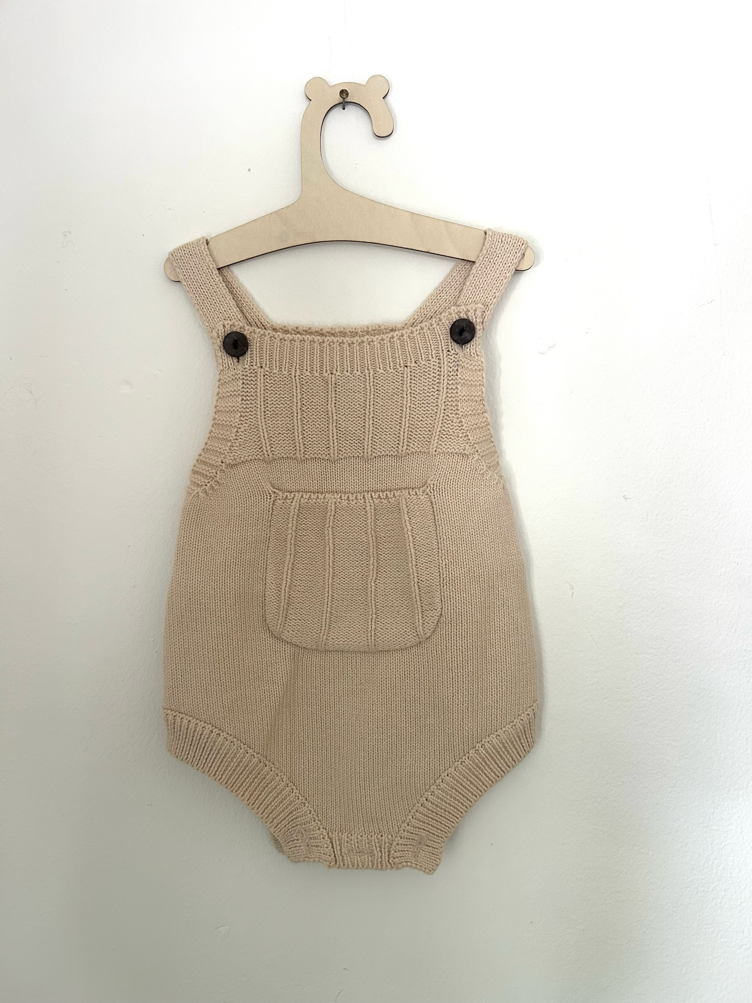 White knit baby romper with 'ONE' text and small bow detail in pink embroidery against hanging clothing background.