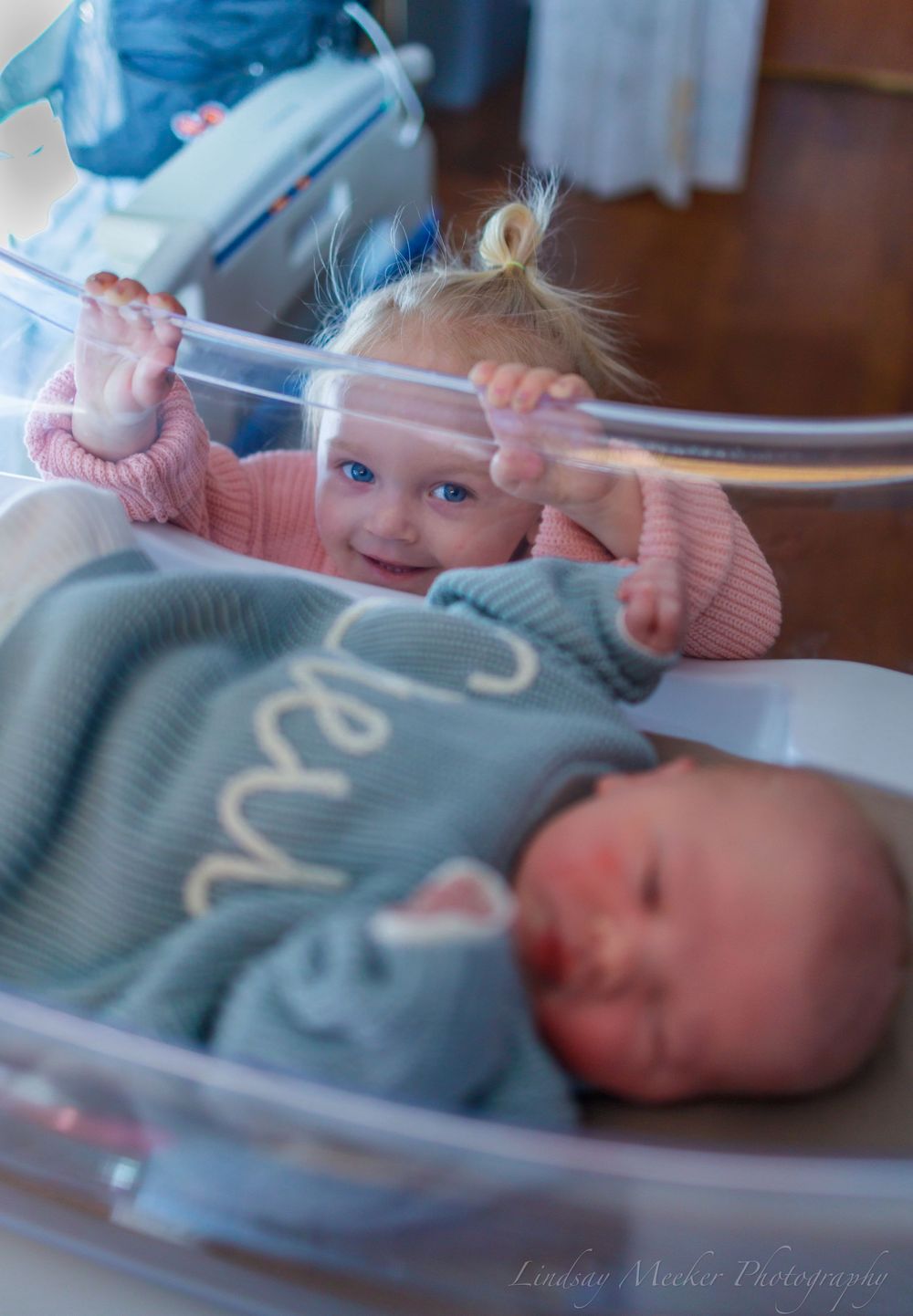Newborn baby in blue knit sweater rests in hospital bassinet.