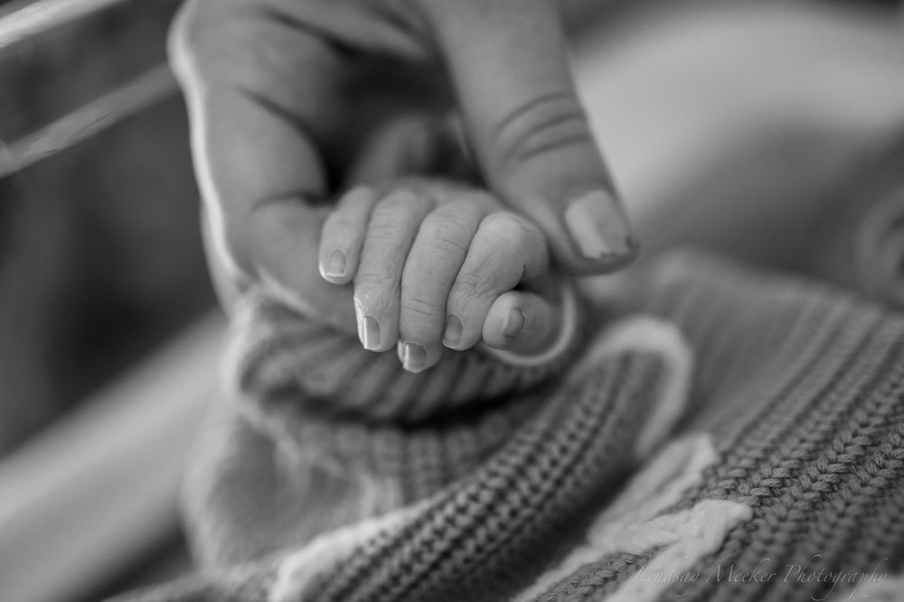 Black and white close-up of tiny newborn hands on textured fabric.