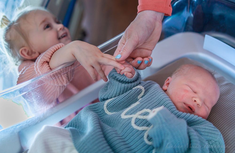 Newborn baby in blue sweater resting peacefully in hospital bassinet.