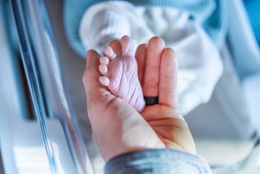 Baby hands reaching up against a blurred blue medical background.