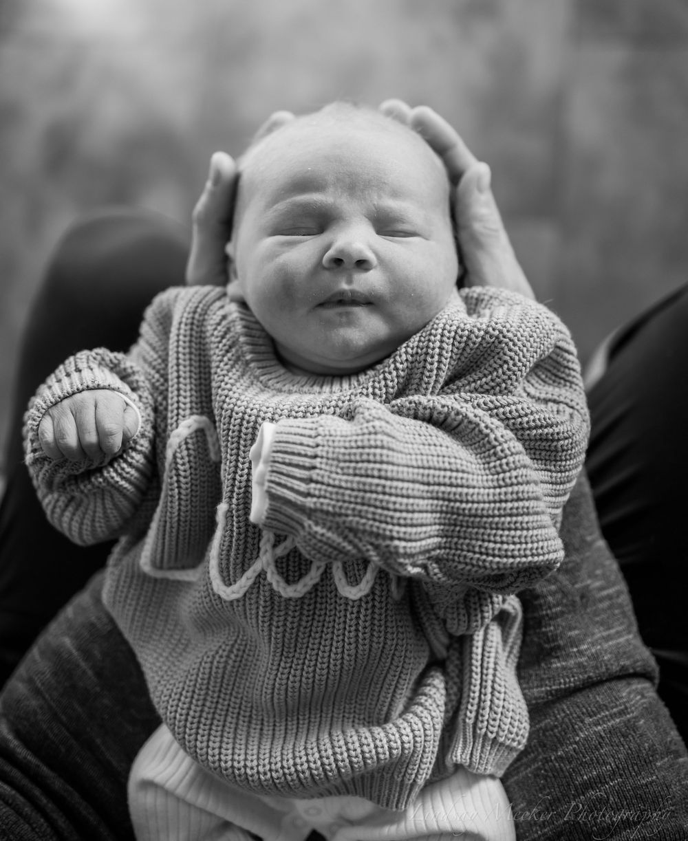 Black and white portrait of newborn baby wrapped in knitted sweater.