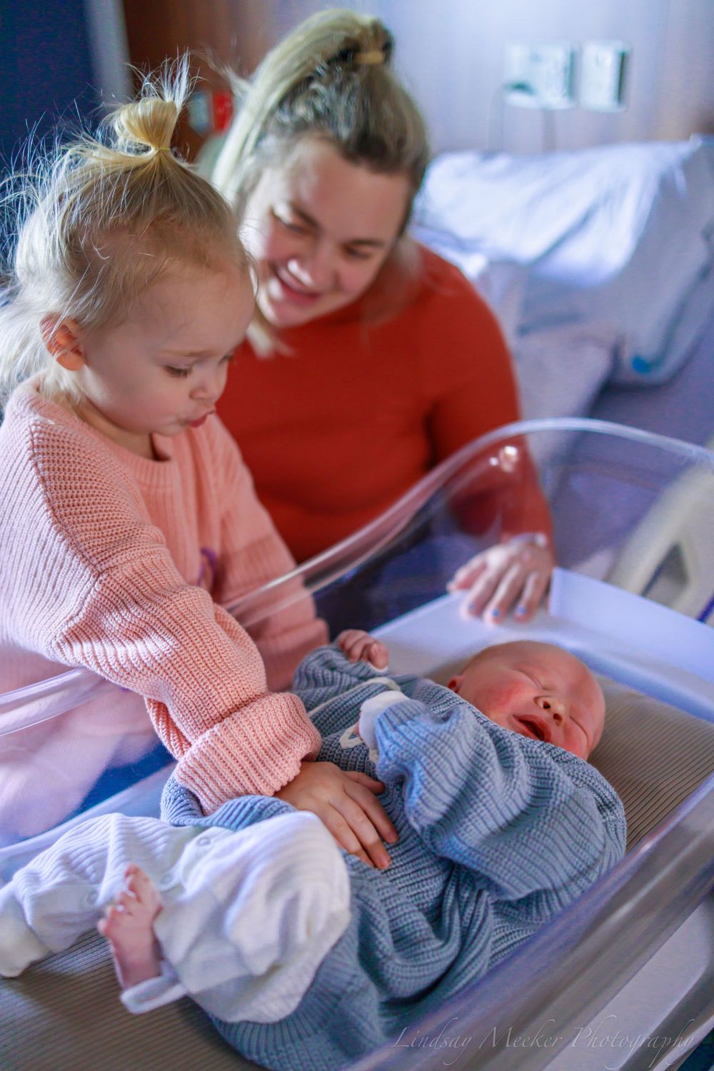 Baby and caregiver interacting over hospital bassinet with knit clothing.
