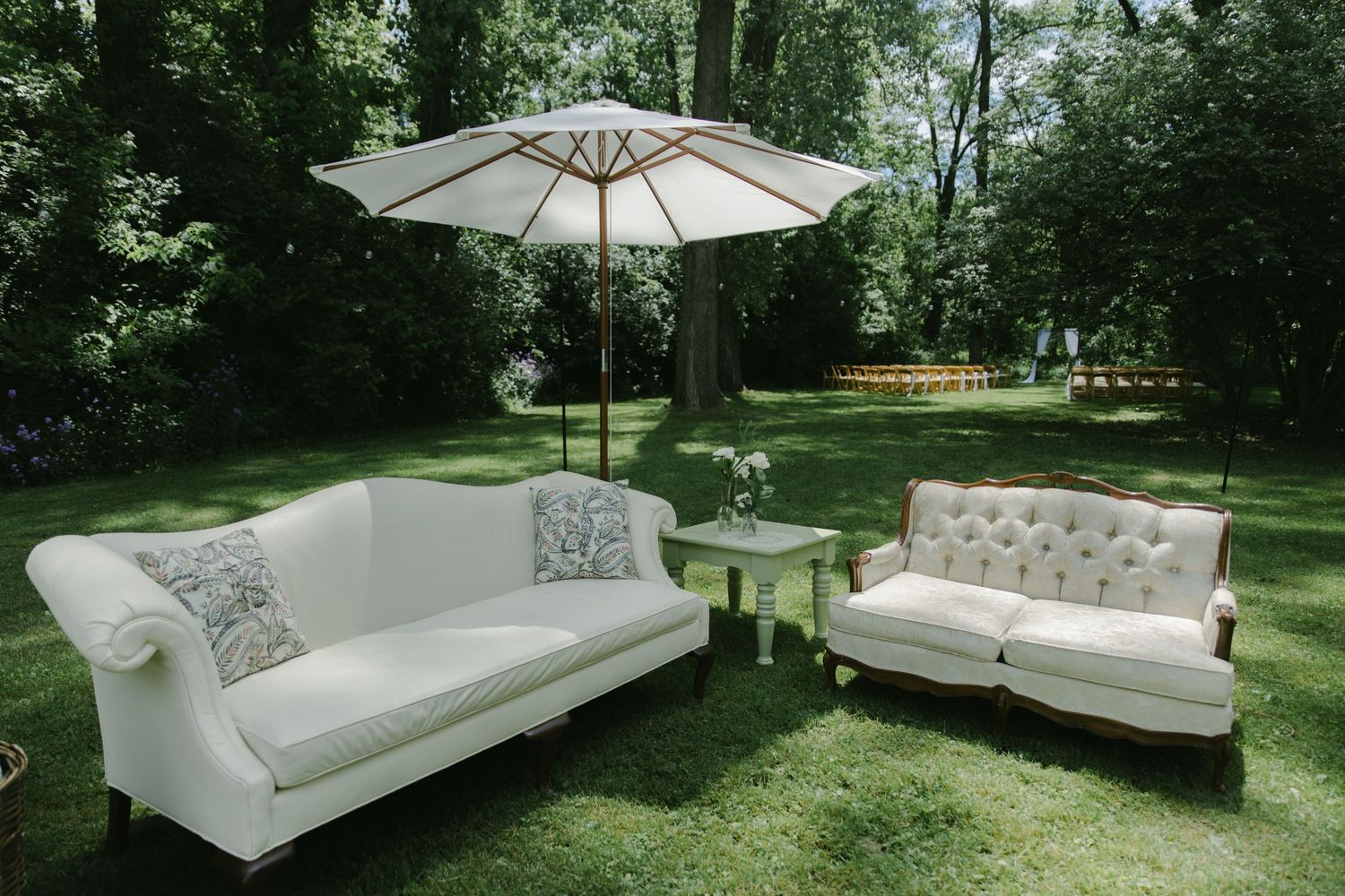 Elegant white vintage sofas and umbrella set up for outdoor wedding lounge area.