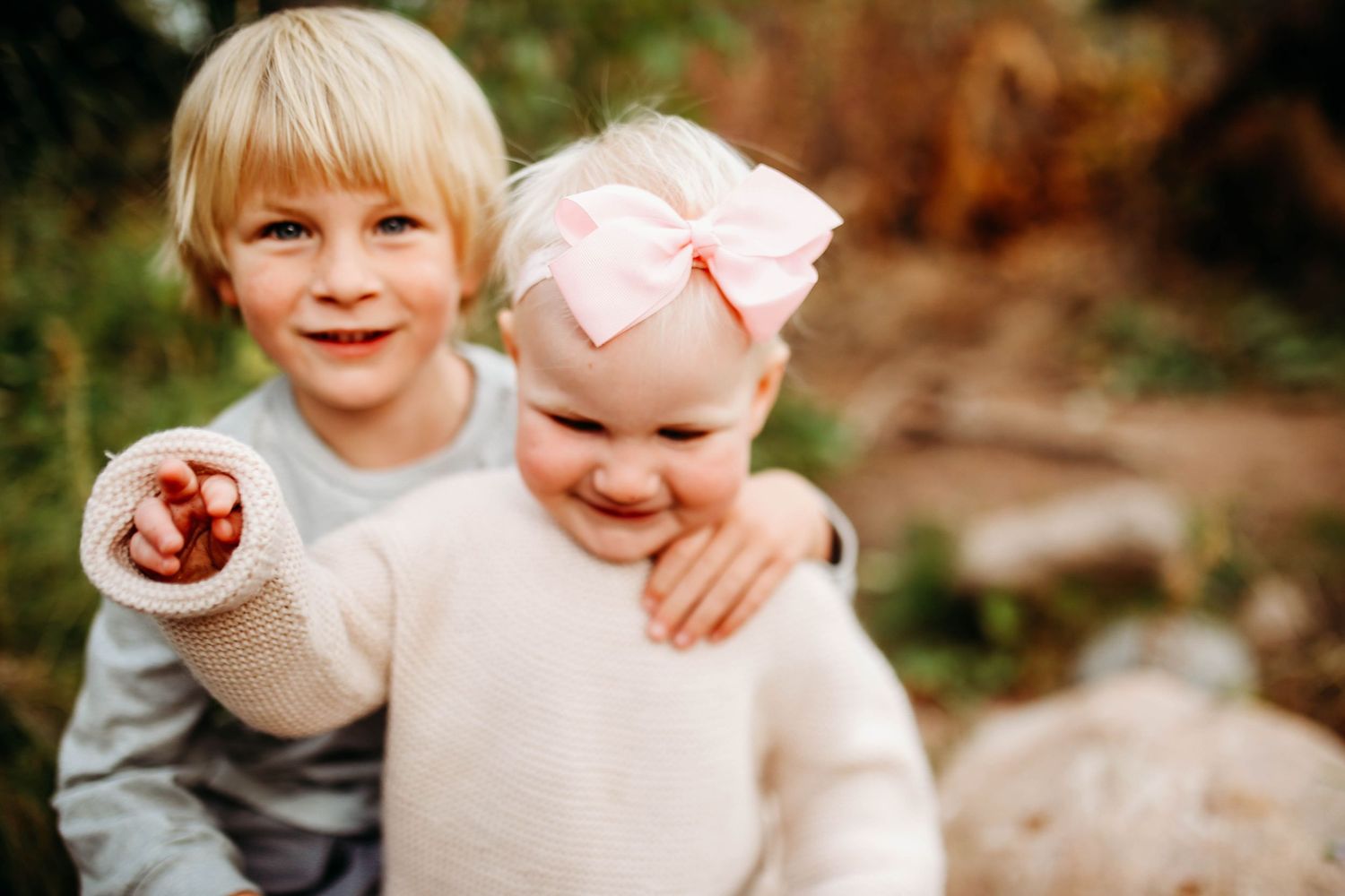 Two children embracing and smiling outdoors in autumn with one holding something in their hand.